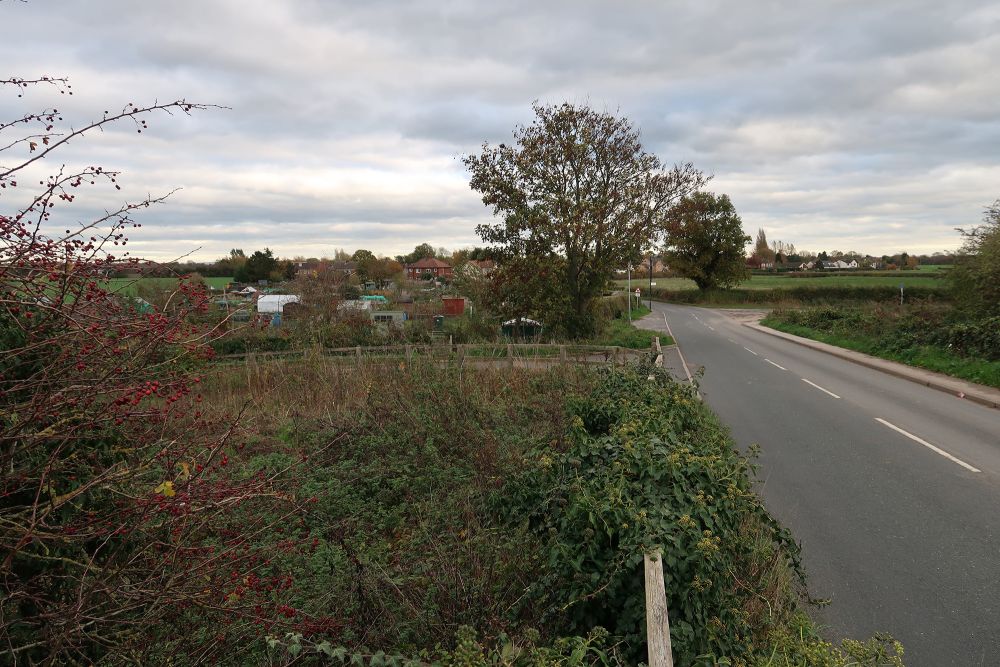 Photograph showng fence-lined fields and a road with a settlement in the distance.