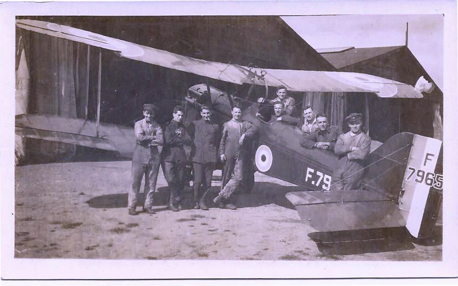 Black and whte photograph of airmen standing in front of a biplane.