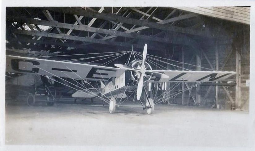 A monoplane stands at the entrance of an aircraft hangar.