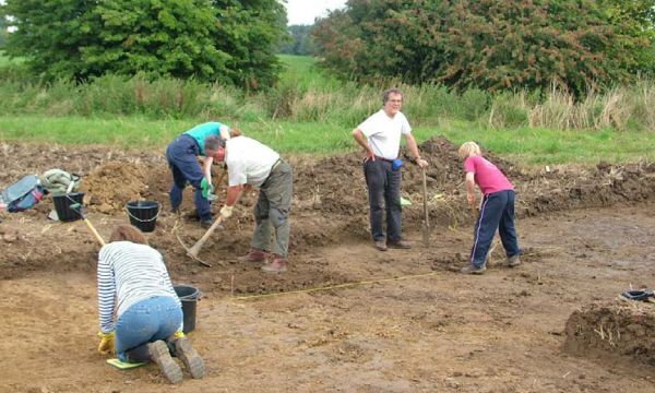 Volunteer archaeologists work with trowels and mattocks on an excavation.