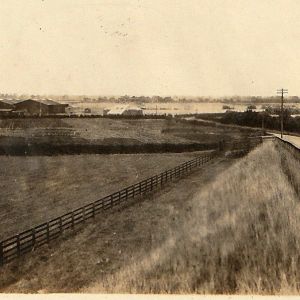 A sepia-tinged photograph of fence-lined fields and a road.