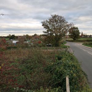 Photograph showng fence-lined fields and a road with a settlement in the distance.