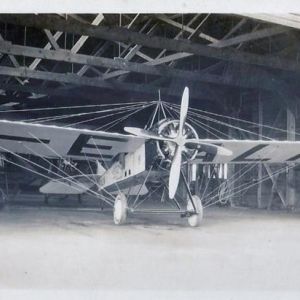 A monoplane stands at the entrance of an aircraft hangar.