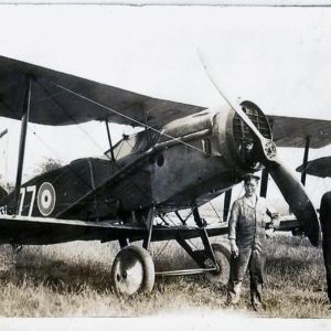 Two young men stand in front of a biplane on an airfield.